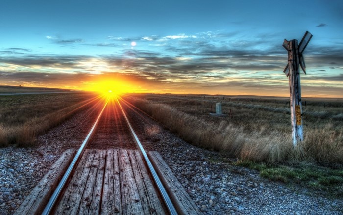 Railroad tracks at sunset with a crossing sign