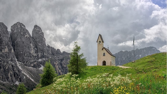 Small church on a grassy hill with mountains and clouds