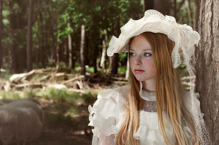 Young woman with red hair and freckles in a white dress in a forest