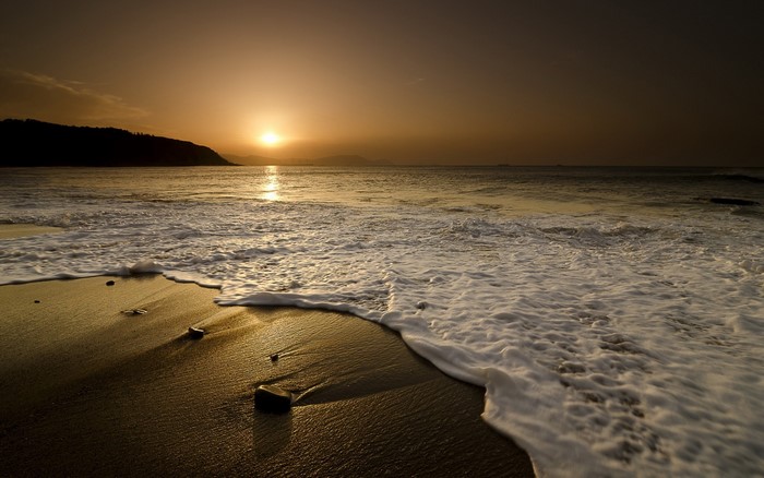 Sunset over the ocean with waves on the shore