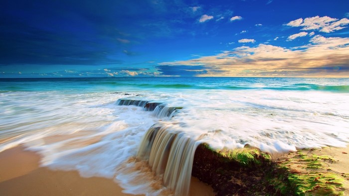 Ocean waves crashing on a sandy beach with rocks