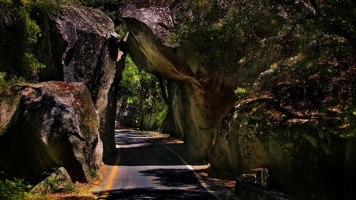 Road passing through a rock archway in a forest