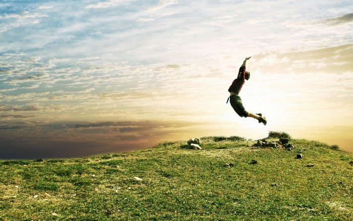 Person jumping on a grassy hill at sunset