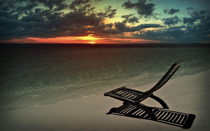 Empty beach chair at sunset over the ocean