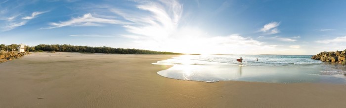 Panoramic view of a beach with surfers at sunset