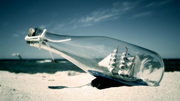 Ship in a bottle on a sandy beach with the ocean in the background