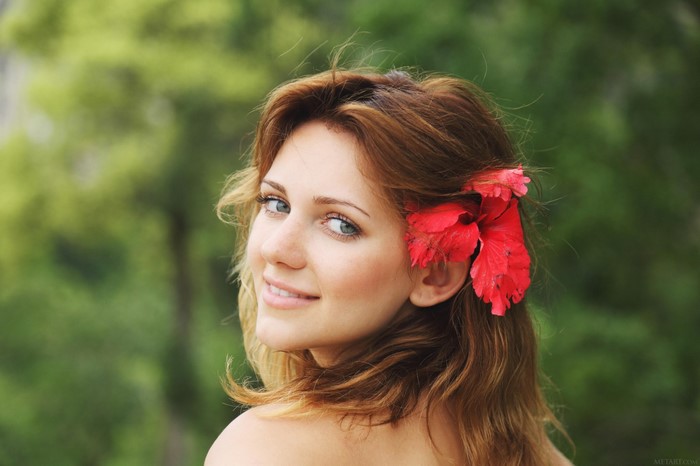 Woman with blue eyes and red flower in brown hair