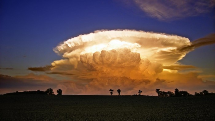 Massive cumulonimbus cloud formation at sunset over a field