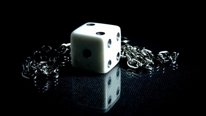 White dice with chain on black reflective surface