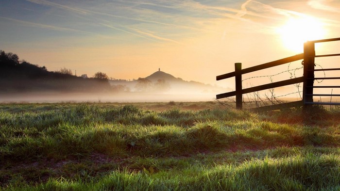 Misty sunrise over a rural field with a fence