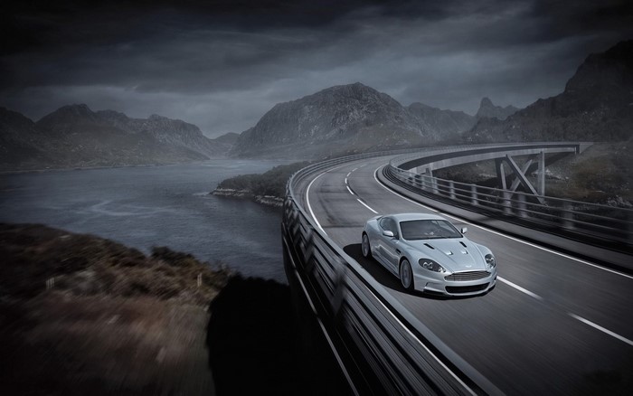 Silver Aston Martin DBS driving on a scenic highway