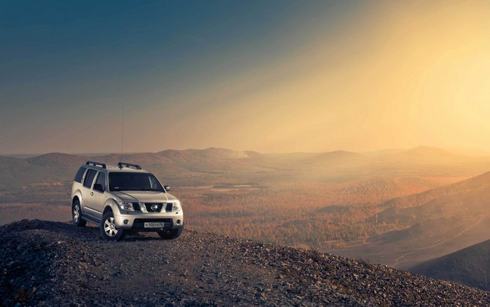 Silver Nissan Pathfinder SUV on a rocky hill at sunset