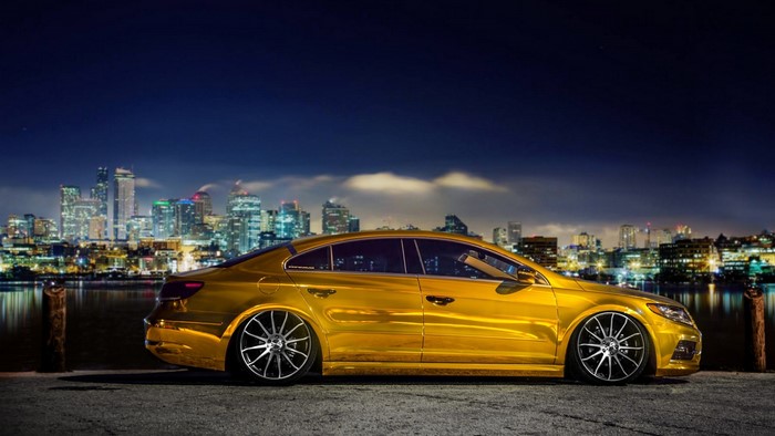 Golden Volkswagen CC parked by a city skyline at night