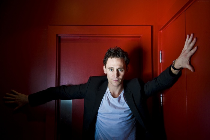Tom Hiddleston leaning against a red door