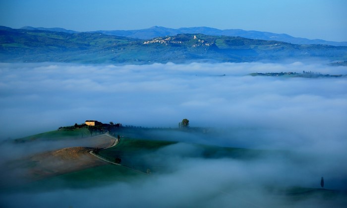 Tuscan landscape with fog and a house on a hill