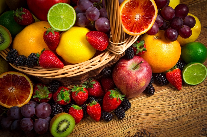 Assortment of fresh fruits in a basket and on a wooden surface