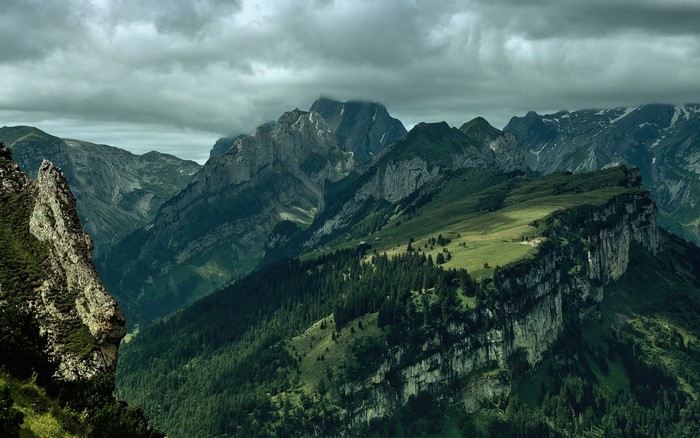 Mountain range with green slopes and rocky peaks under clouds