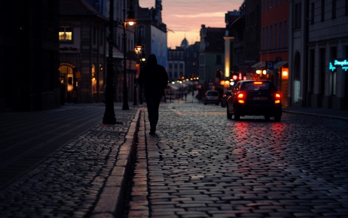 Person walking on cobblestone street at dusk with car