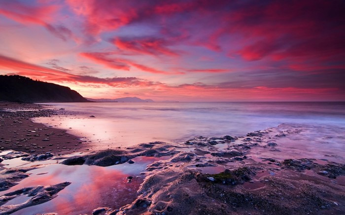 Sunset over the sea with colorful clouds and rocky shore