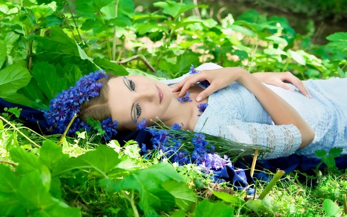 Woman with blue flowers in hair lying in nature