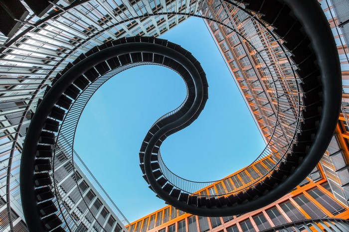Spiral staircase between modern buildings against blue sky