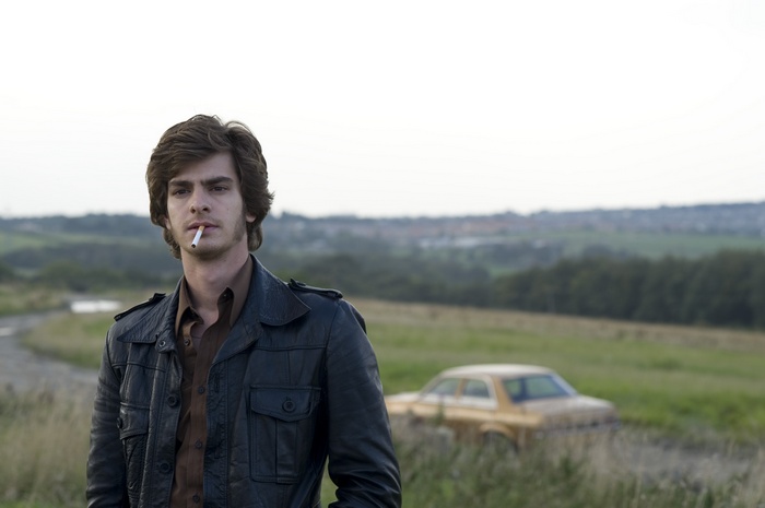Andrew Garfield in a leather jacket smoking a cigarette