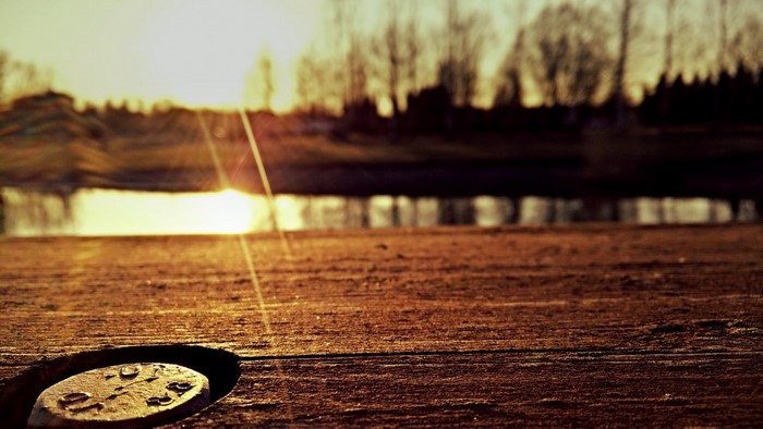 Close-up of a bolt on a wooden surface with sunset reflection on water