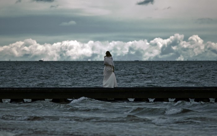 Woman in white dress on pier overlooking the sea