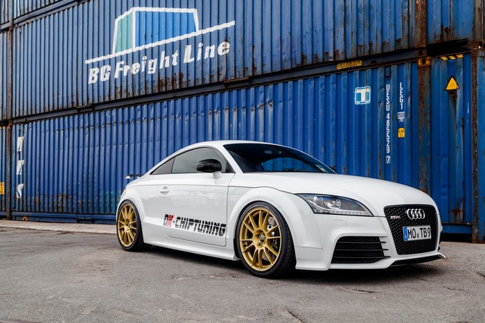 White Audi TT RS with gold rims parked by shipping containers
