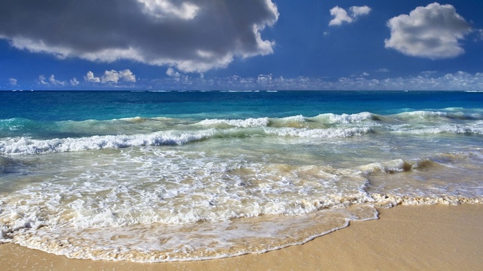 Ocean waves crashing on a sandy beach under a cloudy sky