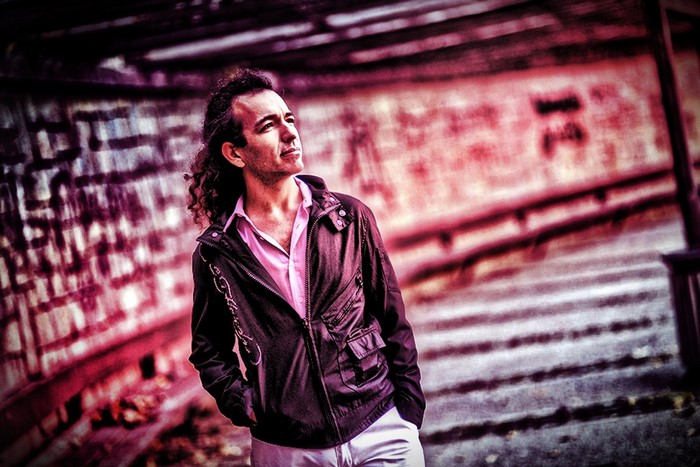 Man with curly hair wearing a pink shirt and black jacket