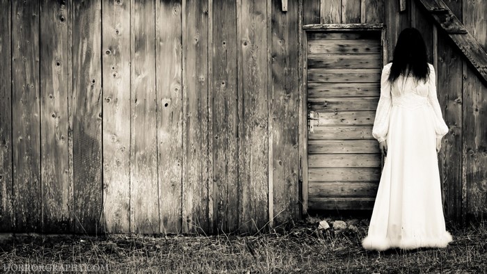 Woman in white dress standing by wooden wall