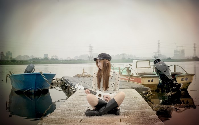 Woman with ukulele on a pier with boats
