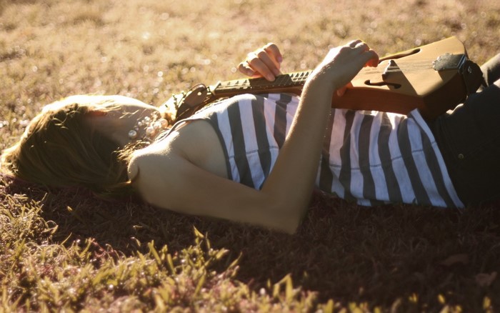 Woman lying on grass playing a musical instrument