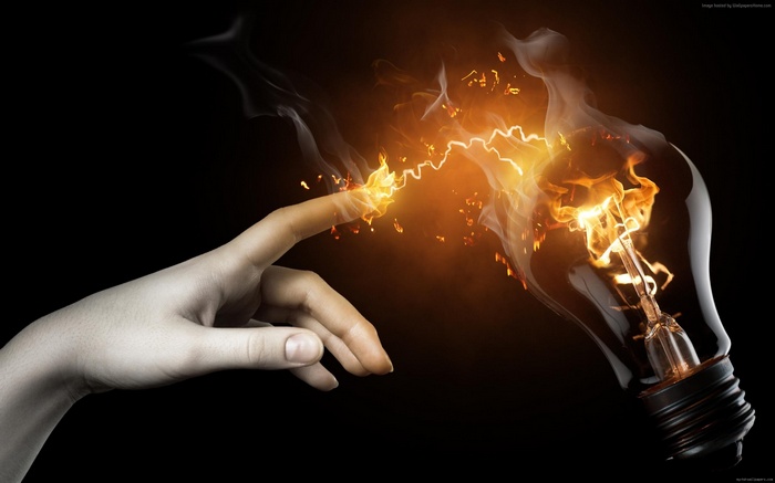 Finger touching a burning light bulb with electricity