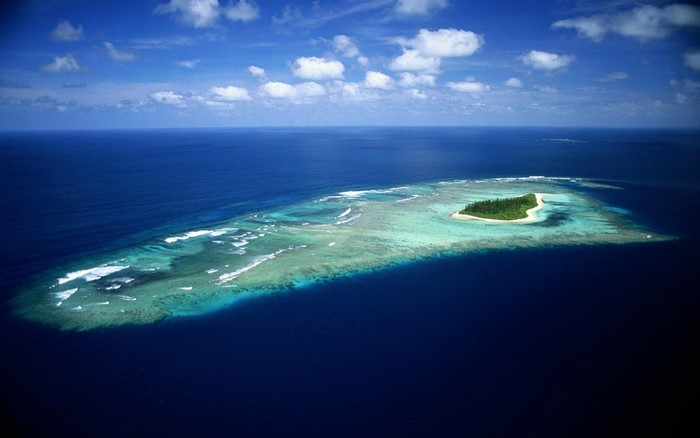 Aerial view of a tropical island surrounded by coral reefs and ocean