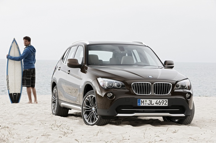 Man with surfboard and BMW X1 on a beach