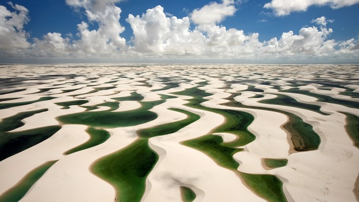 White sand dunes with green lagoons under a cloudy sky