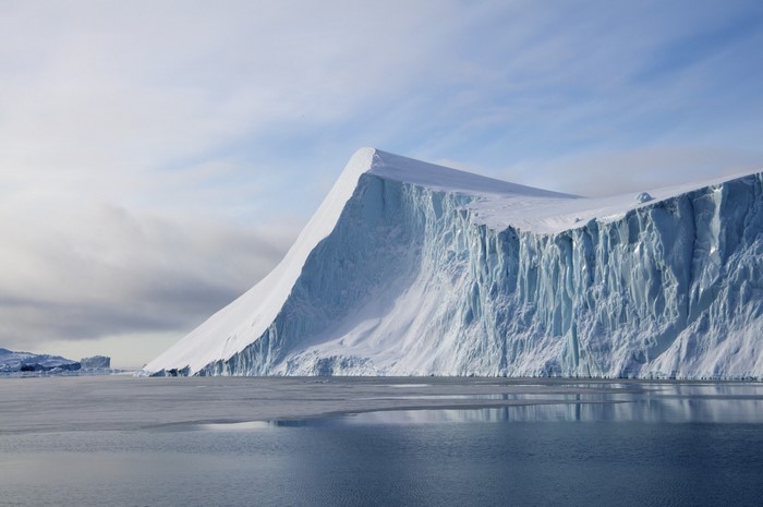 Massive glacier calving into the ocean with icebergs in the distance