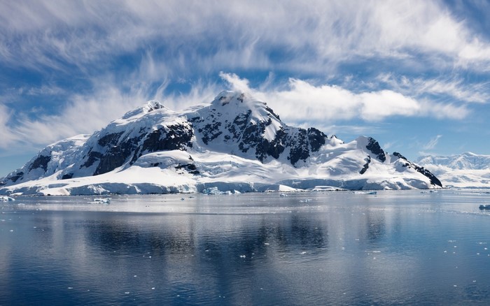 Snow-covered mountains reflected in the sea under a cloudy sky