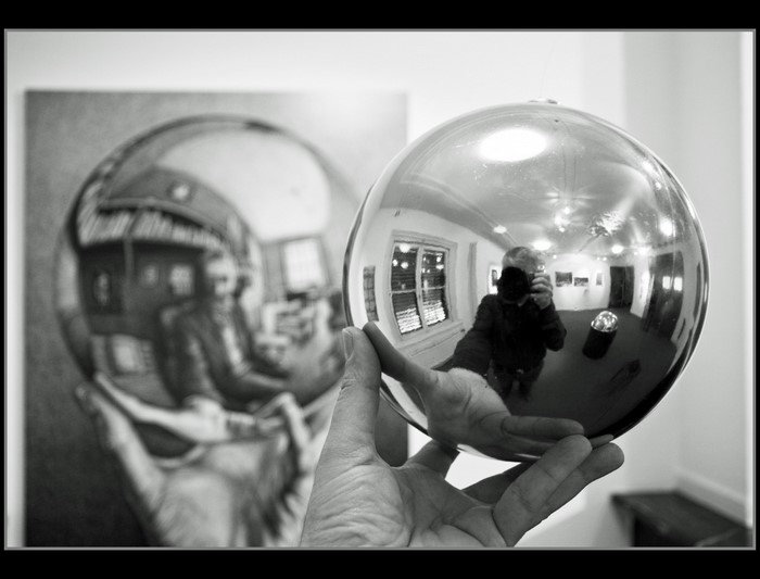 Man holding a reflective sphere showing a self-portrait and a painting