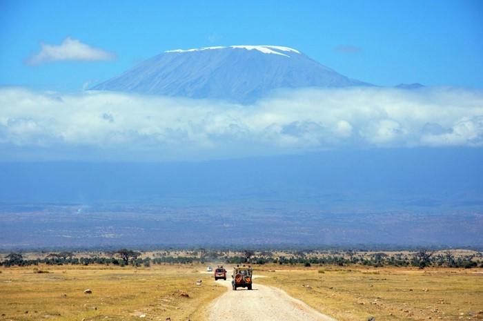 Mount Kilimanjaro above clouds with safari vehicles on a dirt road