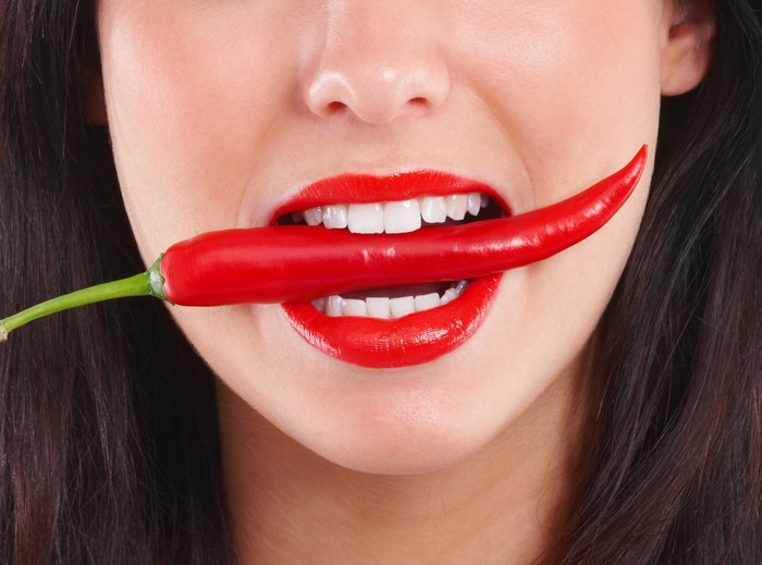 Woman with red lipstick biting a red chili pepper