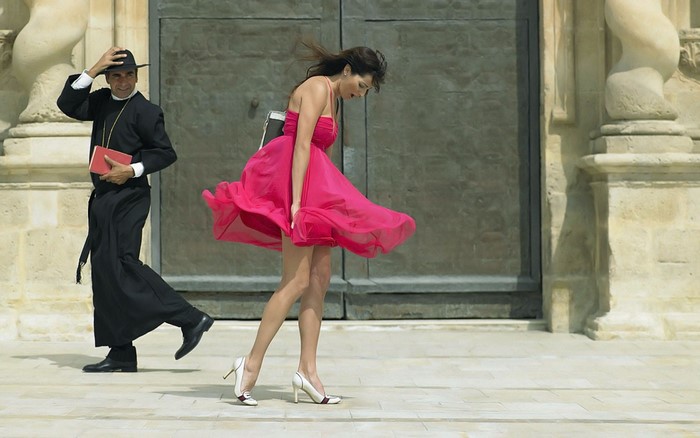 Woman in Pink Dress and Priest in Windy Outdoor Scene