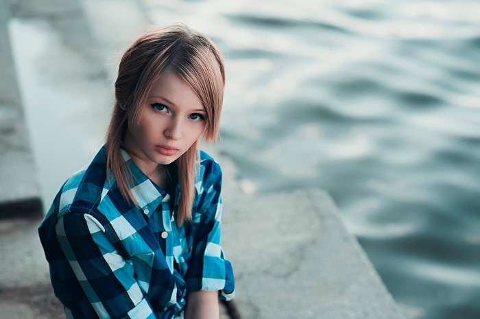 Young woman in blue plaid shirt by water