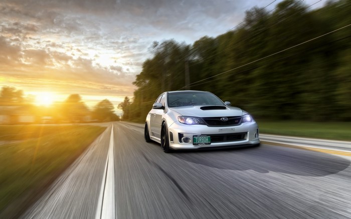 Silver Subaru Impreza WRX STI driving on a road at sunset
