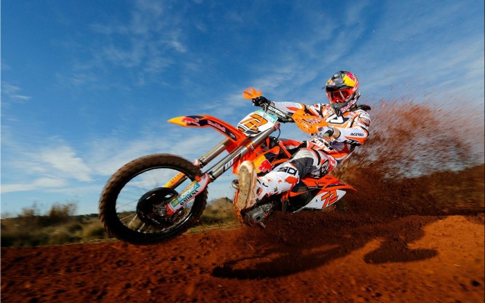 Motocross rider on an orange KTM motorcycle kicking up dirt