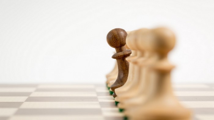 Chess pawns on a board, one dark pawn stands out