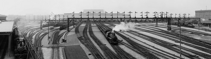 Steam locomotives in a busy rail yard with multiple tracks