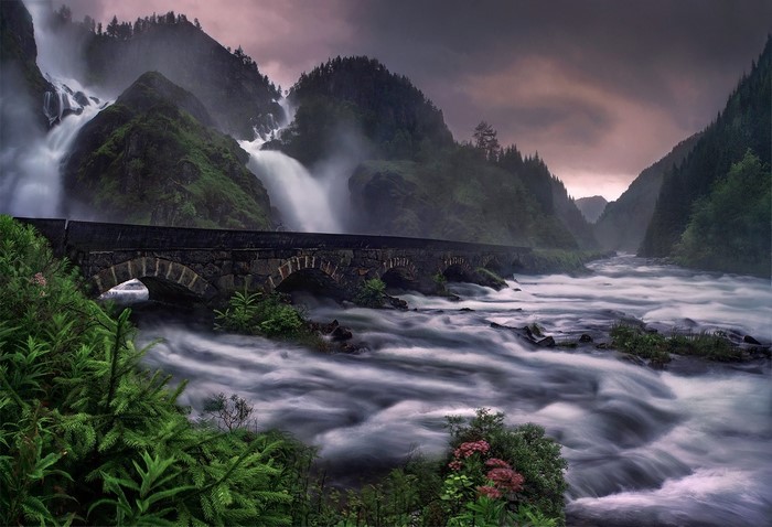 Stone bridge over a river with waterfalls and mountains